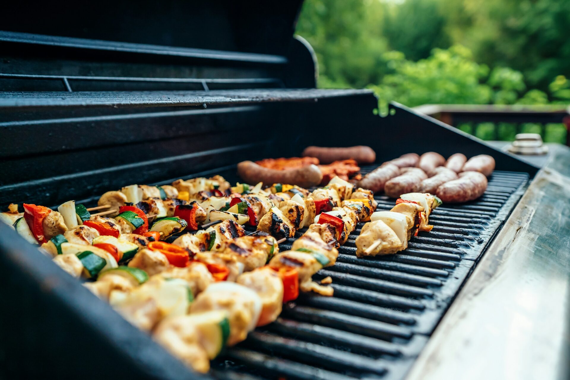An image of some chicken and vegetable kebabs and sausages on a BBQ.