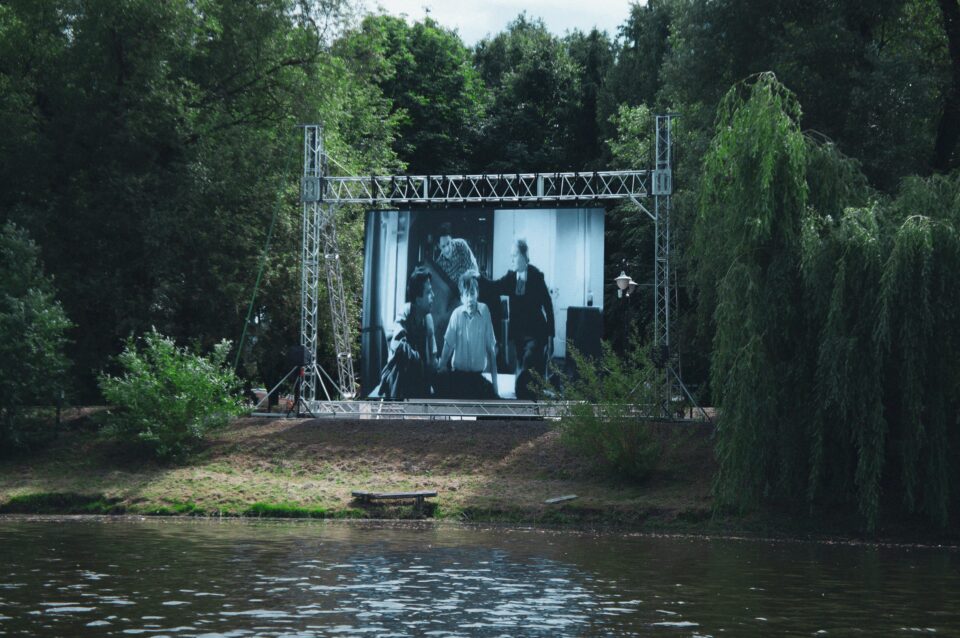 An image of a cinema screen, with a lake in front of it and trees surrounding it.