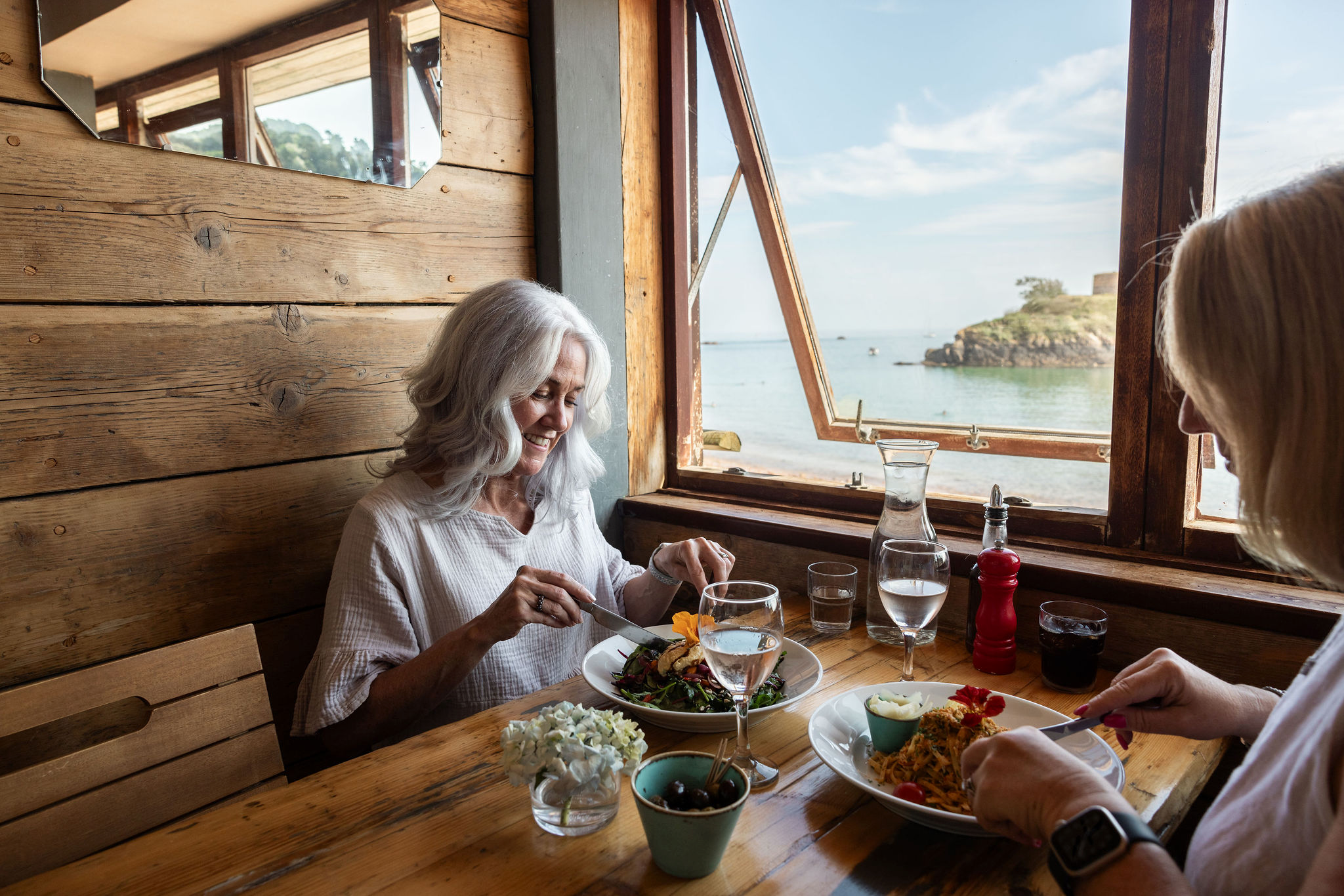 Two people sat inside a restaurant eating a meal by the window.