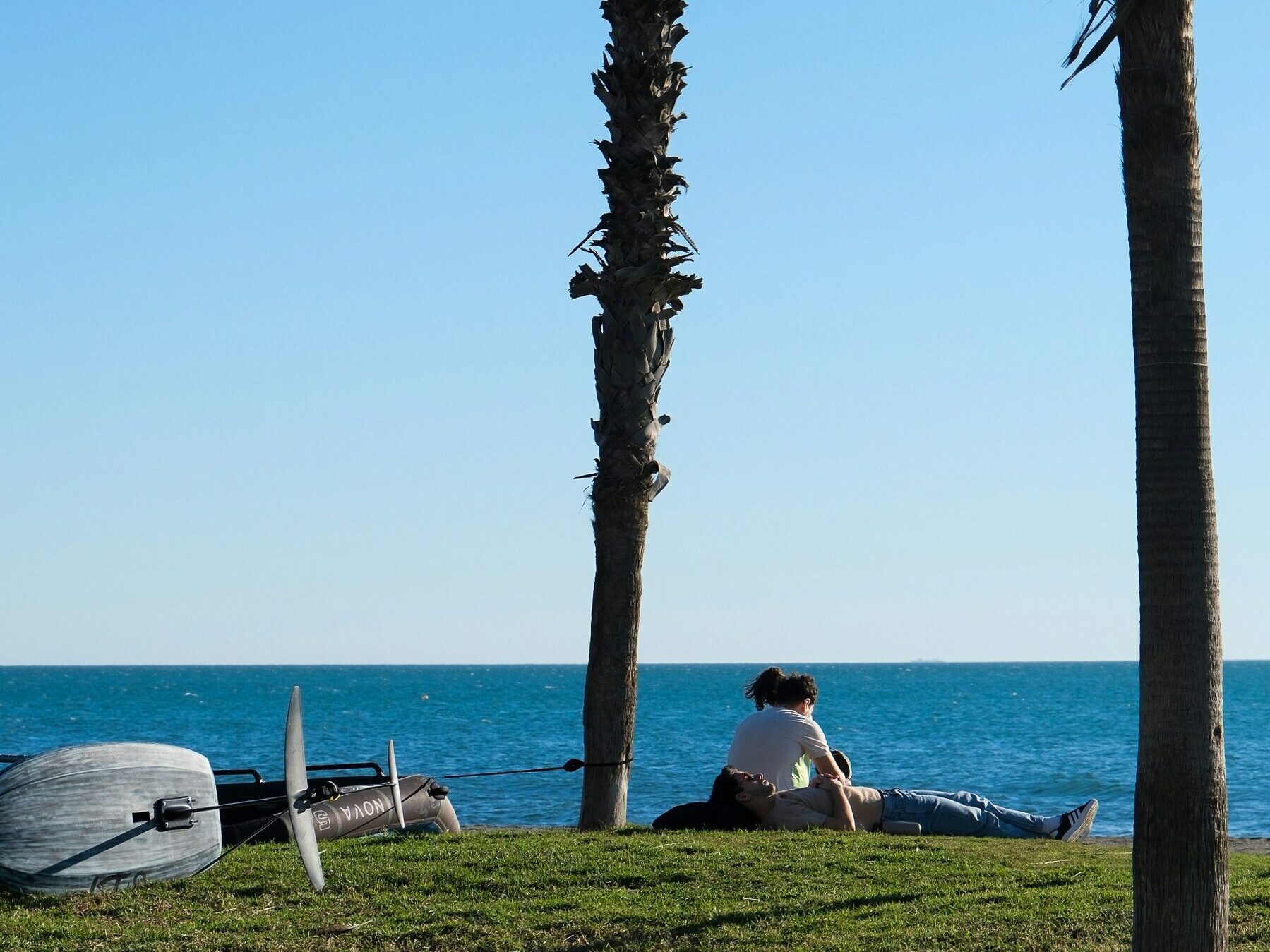 A couple sat on the grass by the sea, in Malaga.