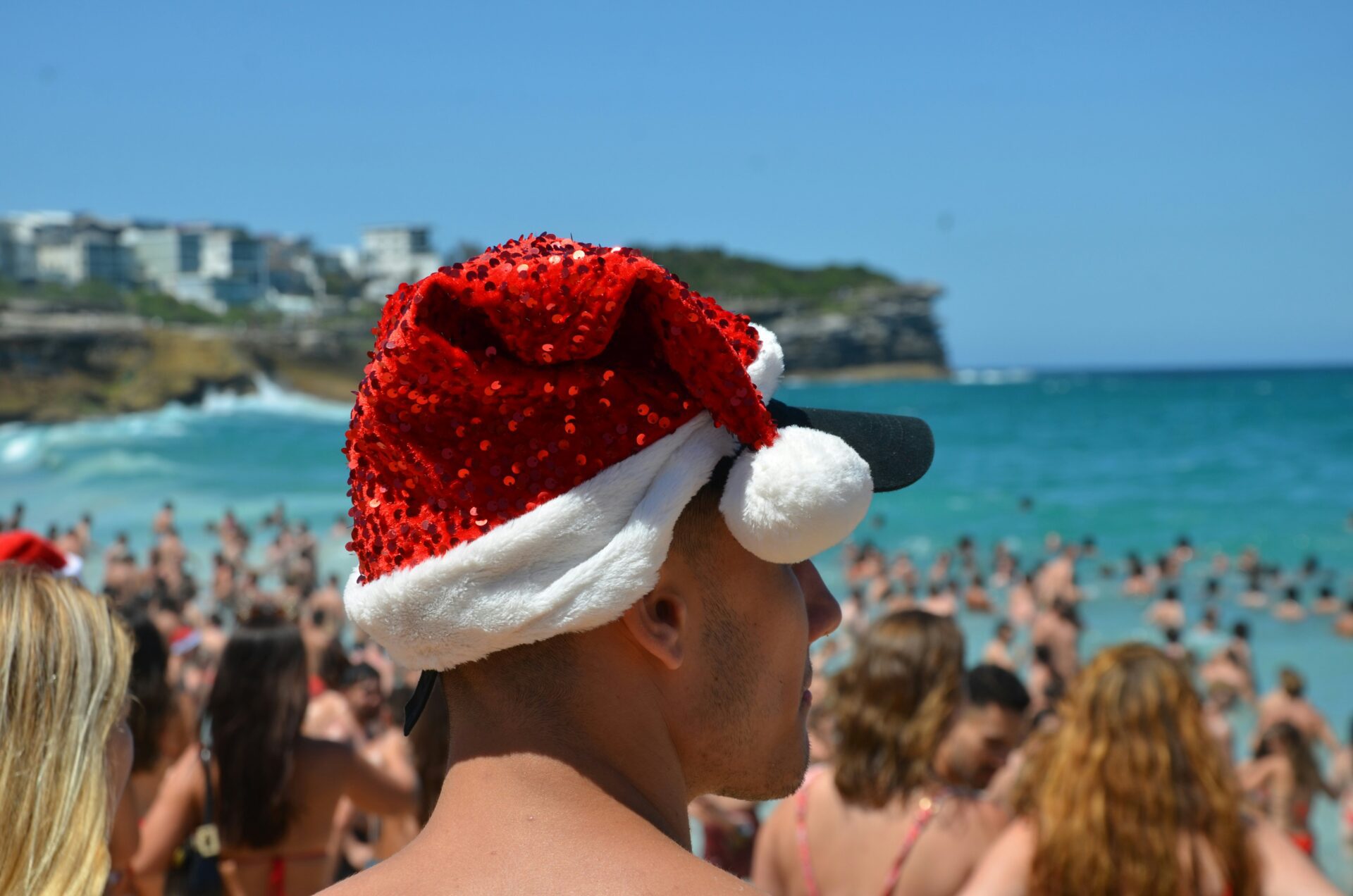 Someone on the beach in the sun with a sparkly red santa hat on